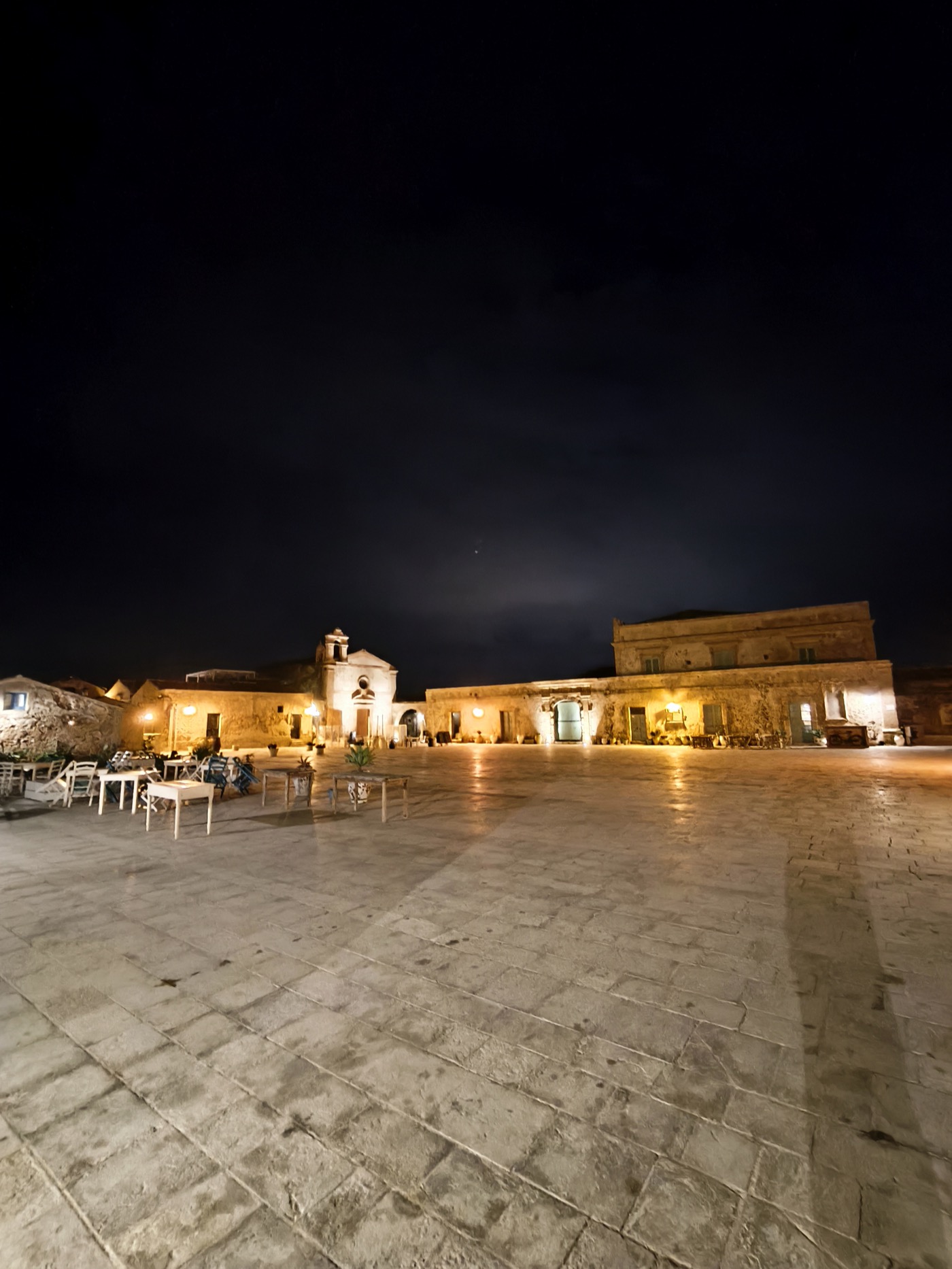 Piazza de Marzamemi la nuit, batiments en pierre chaleureusement eclaires avec tables de restaurant